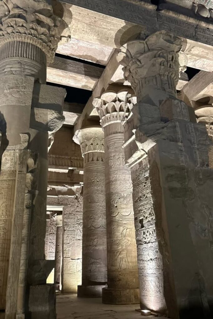 Interior view of Kom Ombo Temple’s hypostyle hall, featuring thick sandstone columns covered in hieroglyphics and illuminated with warm lighting. The preserved details reflect the temple’s significance in ancient Egypt’s religious landscape.