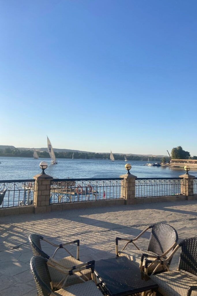 Riverside seating area next to the Nile in Aswan, with wicker chairs, a stone terrace, and traditional sailboats — perfect for travelers exploring luxury hotels in Aswan or looking for authentic things to do in Aswan.