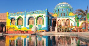 The Anakato Hotel or a similar guesthouse in a Nubian village in Aswan Egypt, with vivid murals of palm trees, desert scenery, and domed architecture reflecting Nubian village culture.