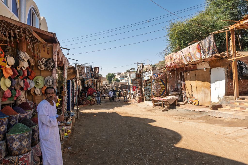 Bustling street in a Nubian village in Egypt with market stalls selling colorful hats, spices, and textiles, capturing the lively atmosphere of a traditional Nubian marketplace in Aswan.