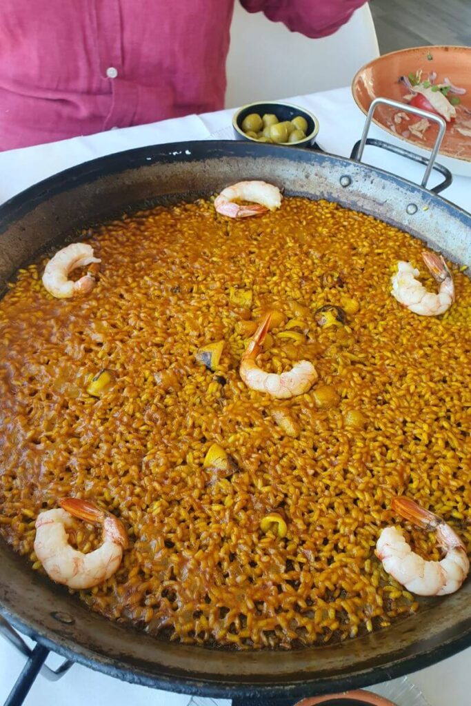Close-up of a large pan of paella with shrimp and golden rice served at a restaurant table. Ideal for illustrating solo dining during travel or enjoying local cuisine alone.
