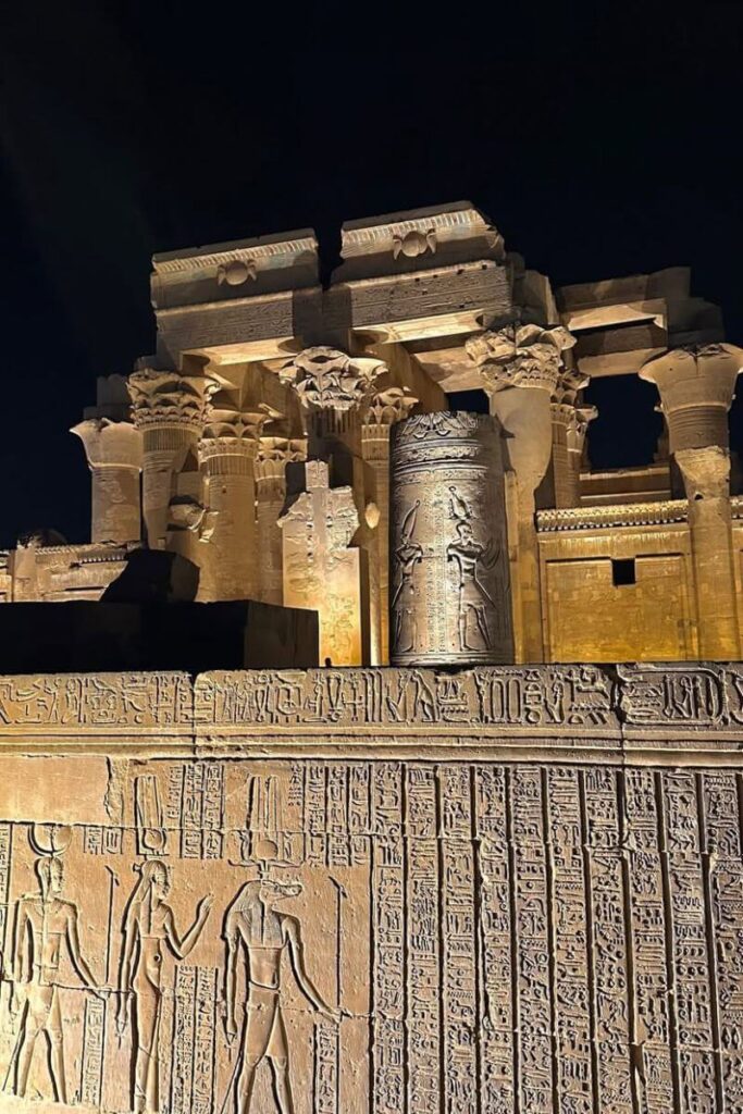 Kom Ombo Temple in Egypt at night, with lit reliefs showing ancient Egyptian deities and inscriptions etched into the stone walls and columns. This dual temple is a must-see stop on temple tours in Egypt.