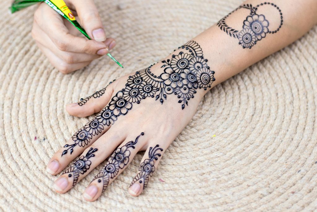 Close-up of a hand with detailed floral henna being applied, set on a woven mat, reflecting popular cultural traditions in Nubian villages. Ideal for visitors to the Nubian village in Aswan, Egypt looking for authentic experiences.