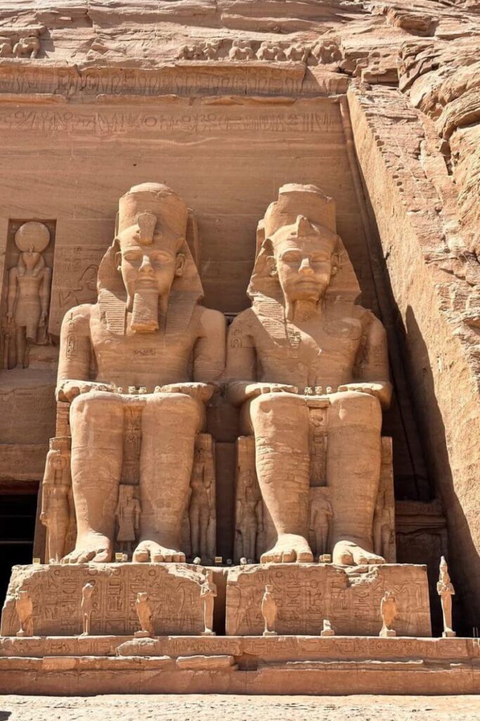 Massive seated statues of Pharaoh Ramses II at the entrance of Abu Simbel Temple with intricate carvings at the base and figures flanking both sides. This iconic image defines the Abu Simbel Temple Egypt experience for day trippers from Aswan.