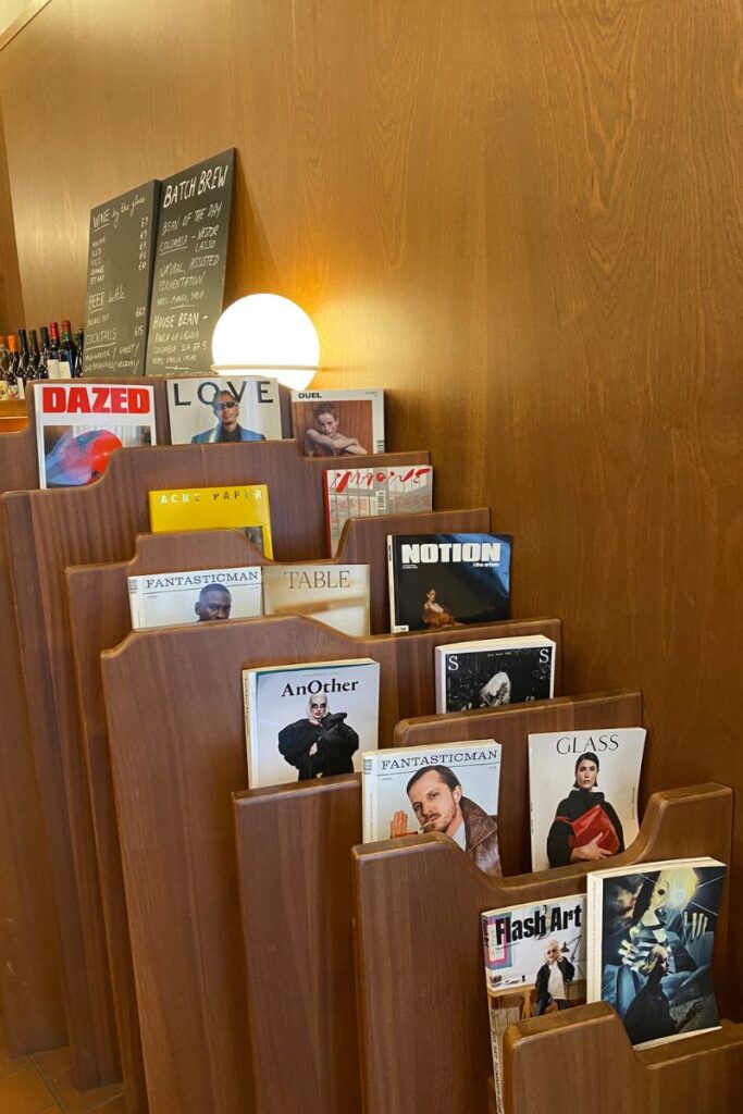 Stylish magazine rack and warm lighting in a modern café, creating an inviting solo restaurant atmosphere. Perfect for sitting alone at a restaurant and practicing the art of eating alone without feeling socially awkward.