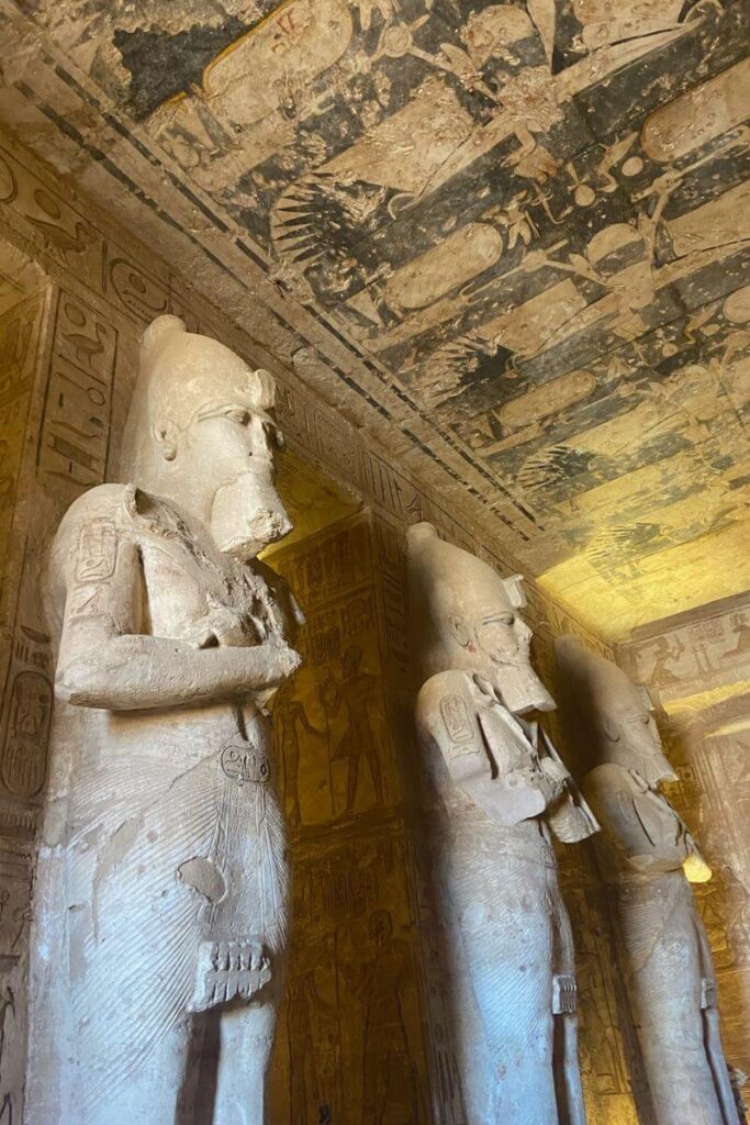 Inside Abu Simbel temple, showing large carved statues of pharaohs beneath an ornate ceiling with ancient Egyptian art — a highlight for those planning travel from Aswan to Abu Simbel and exploring Egyptian heritage.