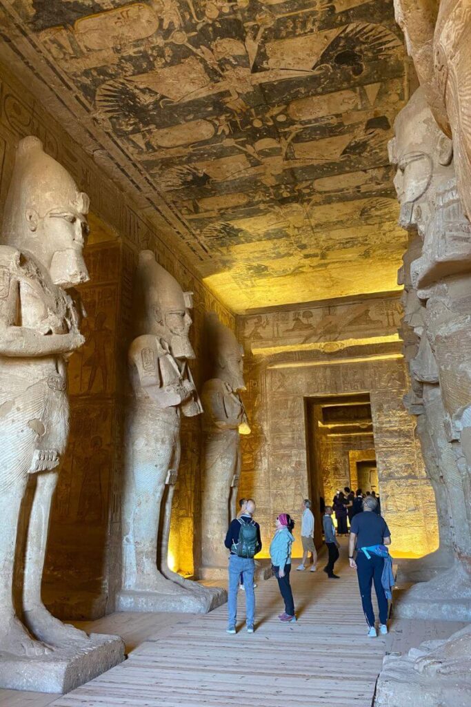 Interior view of Abu Simbel Temple showing massive statues of pharaohs lining the hallway, with tourists walking through. A top highlight in any 2 days in Aswan itinerary and a must-see among the most iconic attractions in Aswan.