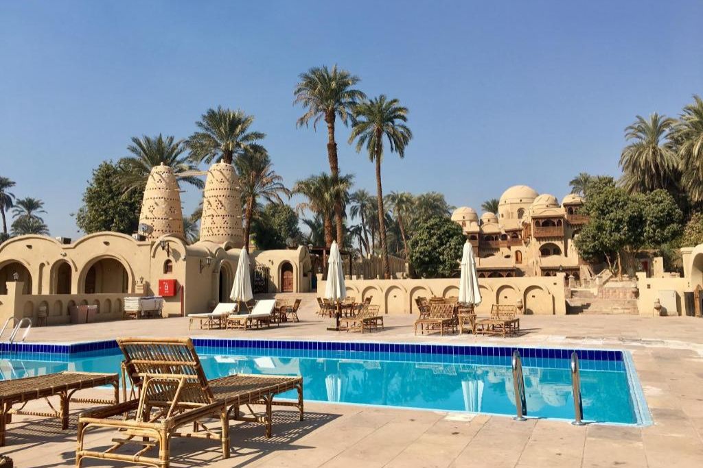 A serene poolside view at a traditional-style hotel in Luxor, Egypt, with tan domed architecture, palm trees, and sun loungers—perfect for travelers searching for unique places to stay in Luxor.