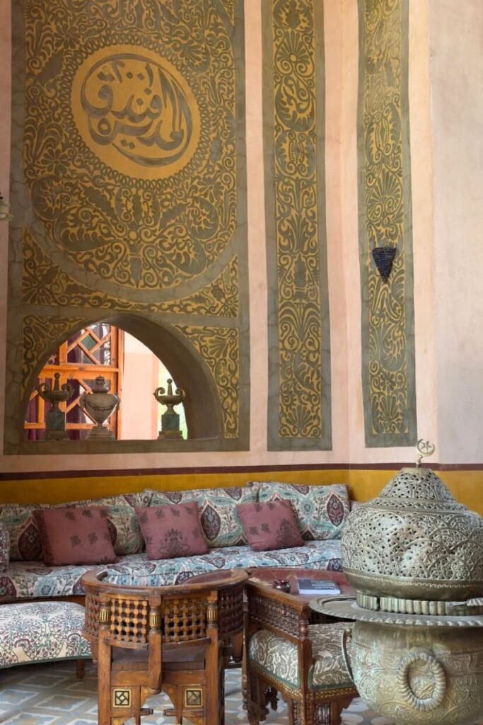 Opulent lounge at a boutique hotel in Luxor, with Arabic calligraphy in gold across high walls, plush patterned cushions, and carved wood furniture. This interior captures the charm of traditional design blended with modern comfort. A perfect example of top boutique hotels in Luxor offering a cultural yet luxurious experience.