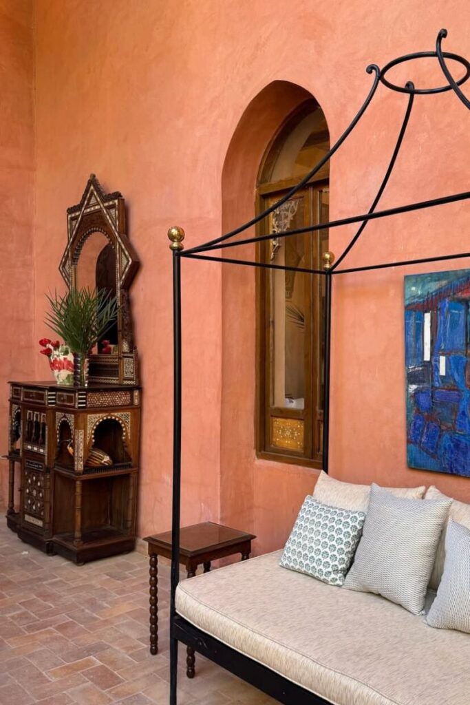 Terracotta-walled patio with a canopy daybed, embroidered pillows, a carved wooden vanity with mirror, and Moroccan-style furniture, bathed in soft natural light. The quiet elegance makes this one of the most visually distinct places to stay in Luxor. Ideal for travelers seeking boutique hotels in Luxor with artistic flair and private lounging spaces.