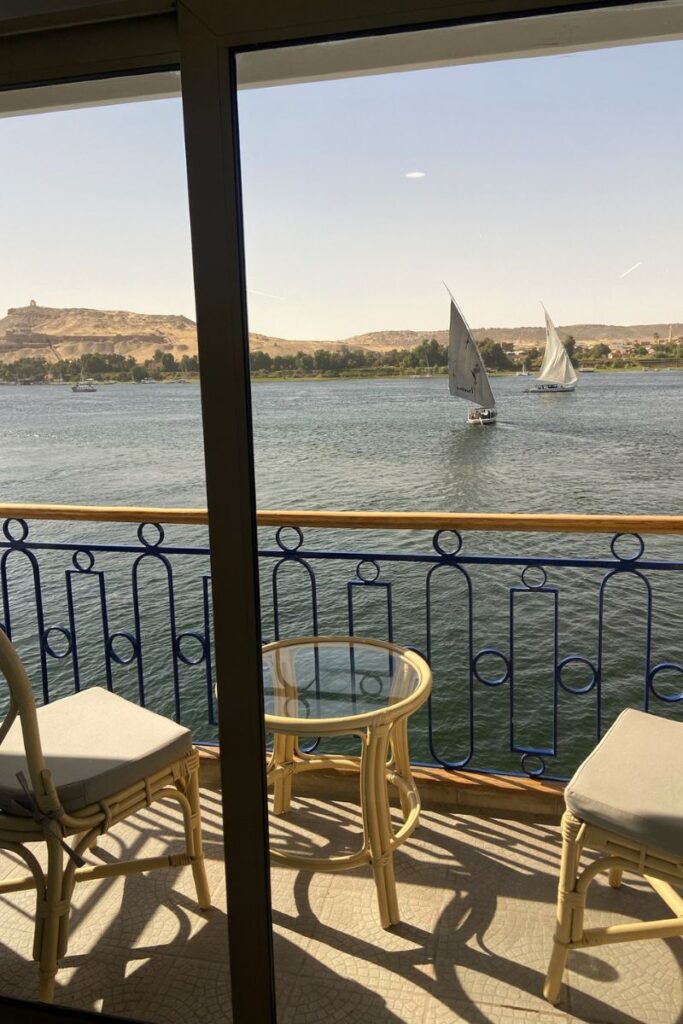 Balcony view from a cruise ship showing two felucca boats sailing on the Nile River, framed by desert hills. Excellent for articles discussing felucca Nile cruise options, traditional sailing, or cruises from Luxor to Aswan.