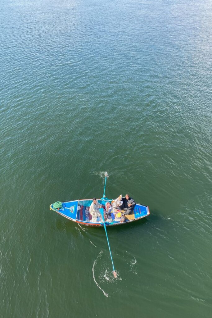 A small wooden boat with three men selling goods, paddling near a larger cruise ship on the Nile. Perfect for illustrating local encounters on Nile cruises from Aswan to Luxor or exploring as part of an Egyptian cruise adventure.