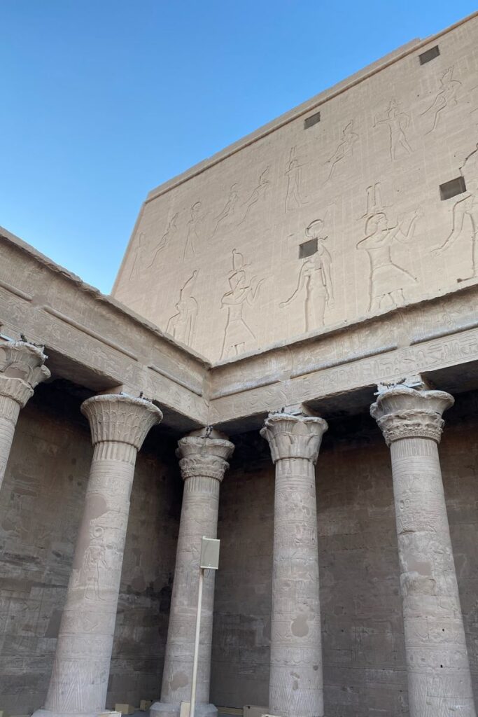 Stone columns and walls with engraved Egyptian figures under clear blue sky. No visible text. A classic example of temples at Luxor and top-rated attractions in Luxor Egypt.
