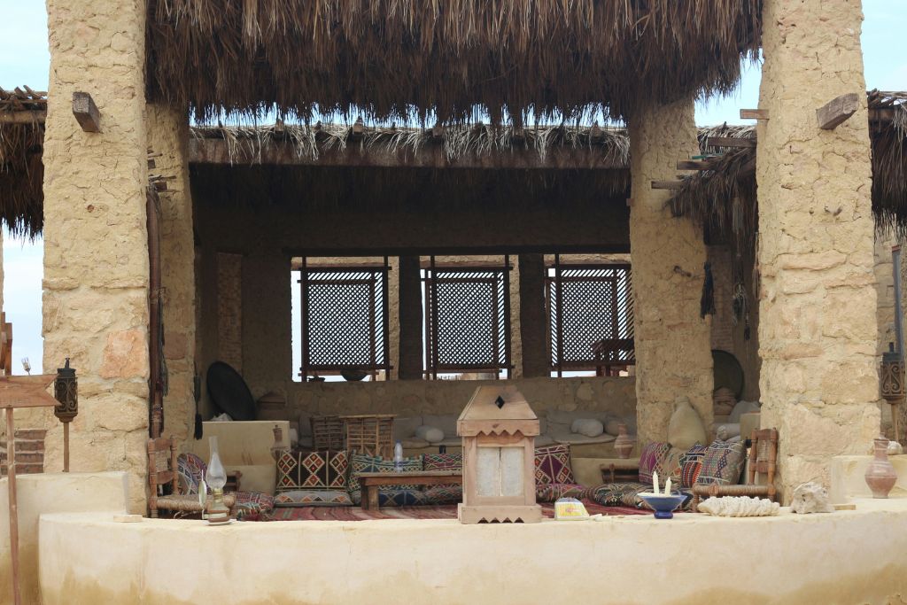 Cozy open-air seating area at a Siwa Oasis hotel, with patterned cushions, rustic decor, and a traditional thatched roof—an inviting space that reflects the charm of hotels in Siwa Oasis and authentic Siwa Egypt hospitality.