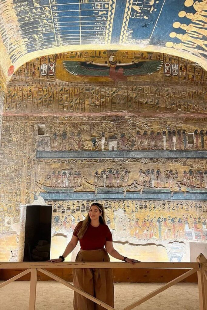 nterior of a richly decorated tomb in the Valley of the Kings with a blue and gold vaulted ceiling and extensive wall murals. A visitor stands below, emphasizing the scale and beauty of one of the best tombs in the Valley of the Kings open to the public.