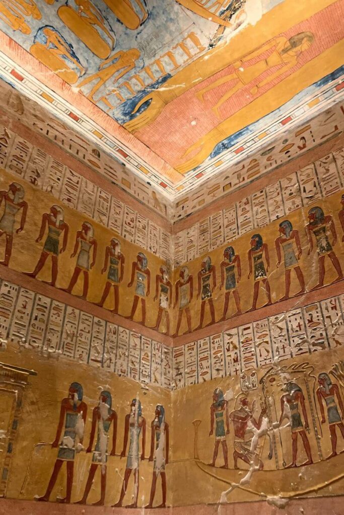 A vibrant wall painting inside one of the tombs in Luxor Valley of the Kings, showing rows of standing figures dressed in traditional garments, interspersed with hieroglyphic inscriptions. The vivid colors and detailed figures highlight the craftsmanship and history within Egypt Valley of the Kings tombs.