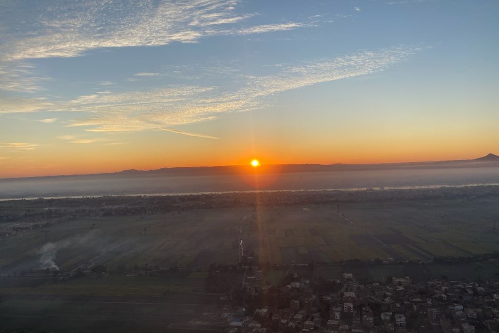 A dramatic sunrise casts golden light over Luxor’s landscape and Nile River, as seen from a hot air balloon in Egypt. The image beautifully captures the serenity and majesty of an early morning Luxor balloon ride.
