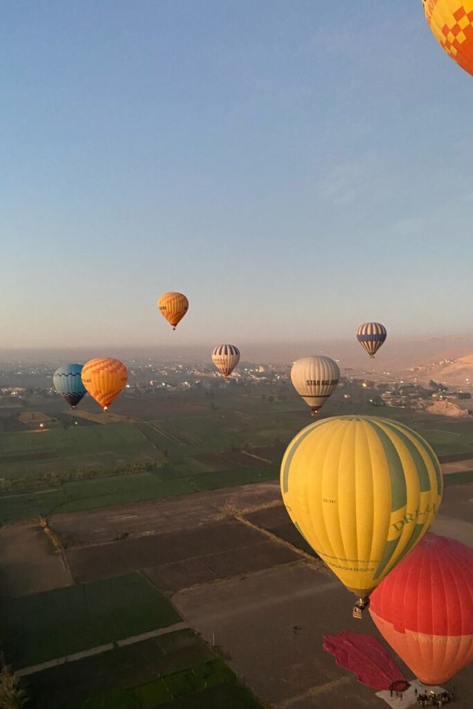 A stunning aerial view of balloons floating over farmland and open desert at sunrise in Luxor, Egypt. This image captures the essence of a Luxor adventure and the thrill of seeing Egypt from the sky.