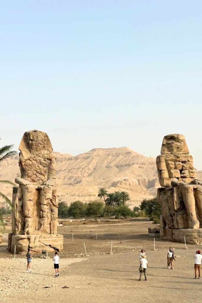 Tourists gather around the towering twin statues known as the Colossi of Memnon, set against the backdrop of the Theban mountains. This is one of the top places to visit in Luxor Egypt and an easy stop during a West Bank tour.