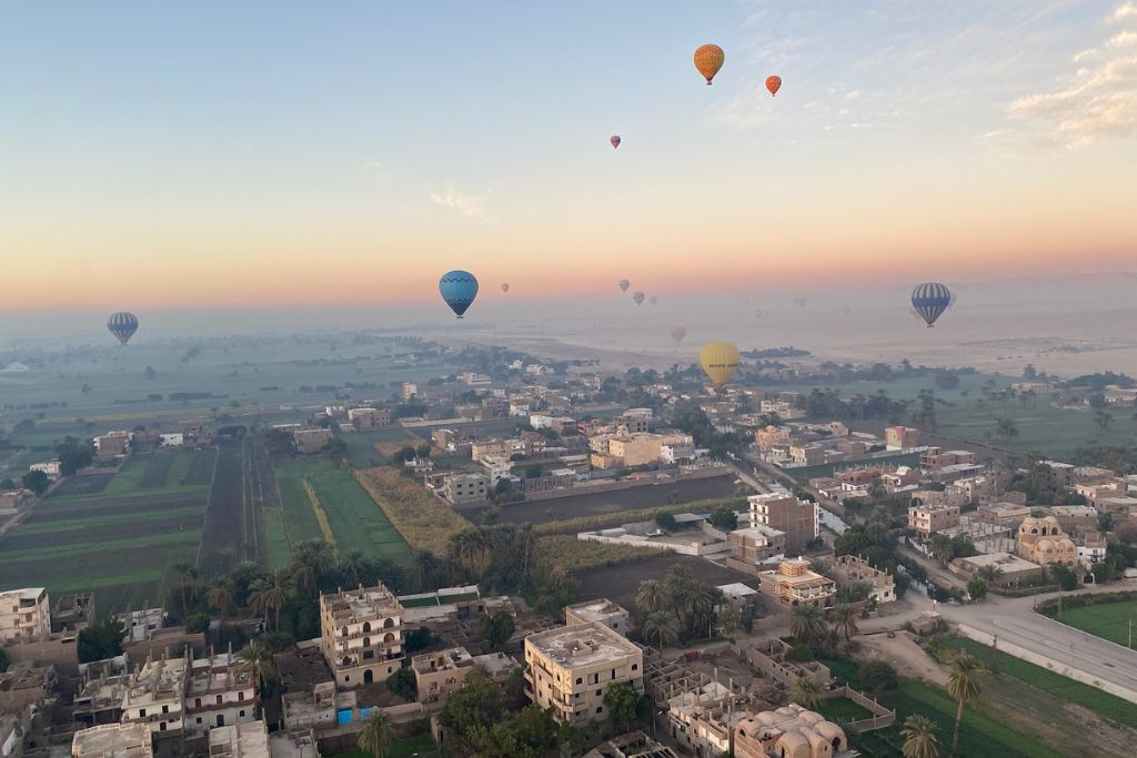 An aerial view of Luxor’s farmland and residential buildings at sunrise, dotted with colorful hot air balloons. This is a classic perspective from a hot air balloon Luxor Egypt is famous for.