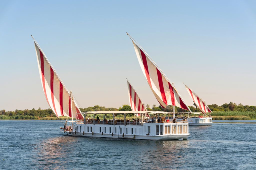 White cruise boats with red and white striped sails on the Nile River near Luxor—Nile sailing is a classic experience during a Luxor tour.