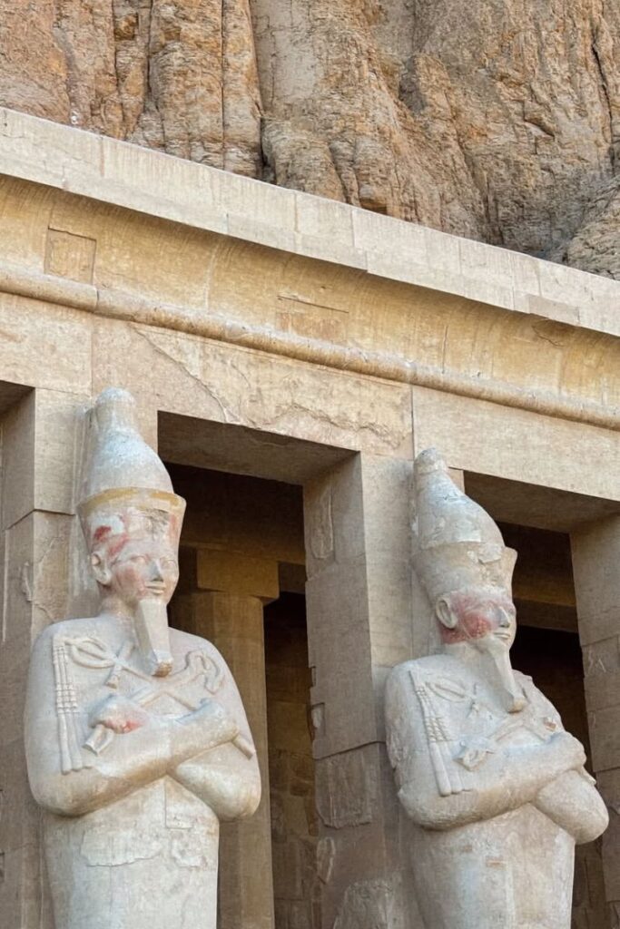 Close-up of two statues at the Mortuary Temple of Hatshepsut, still showing remnants of red pigment on their faces. This is one of the most visually striking and historic places to see in Luxor Egypt.