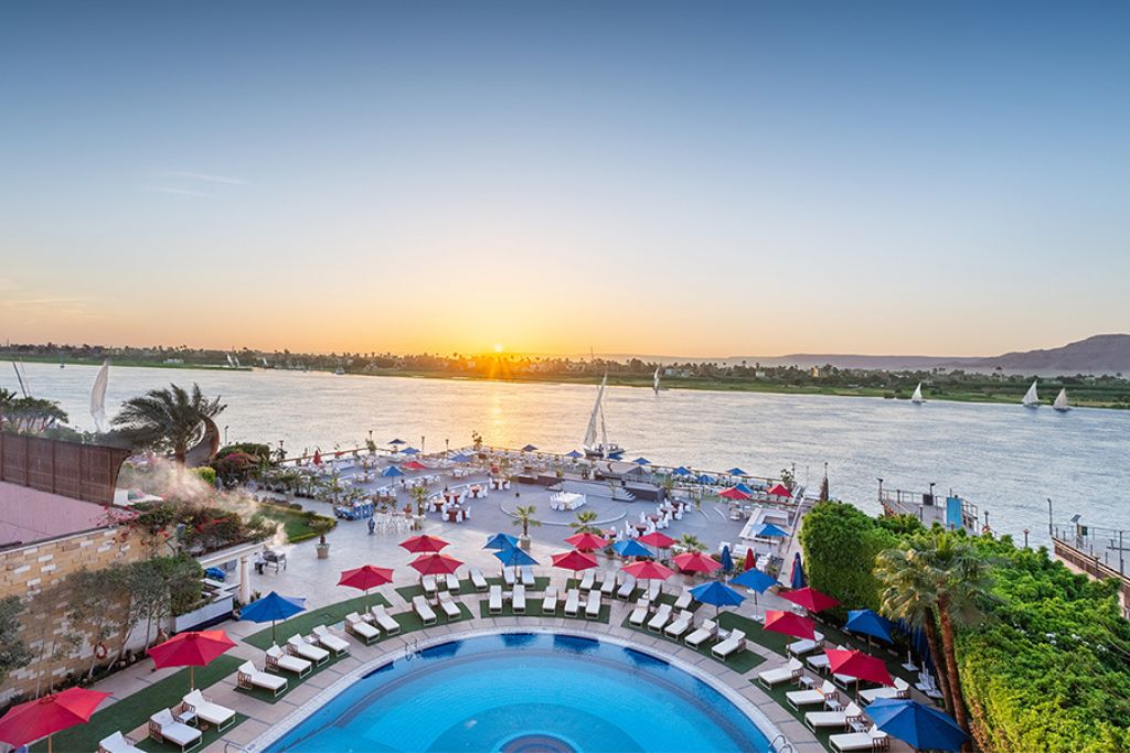 Resort pool deck at sunset along the Nile River in Luxor, lined with white loungers and colorful umbrellas—showcasing one of the best hotels in Luxor Egypt with spectacular riverfront access.