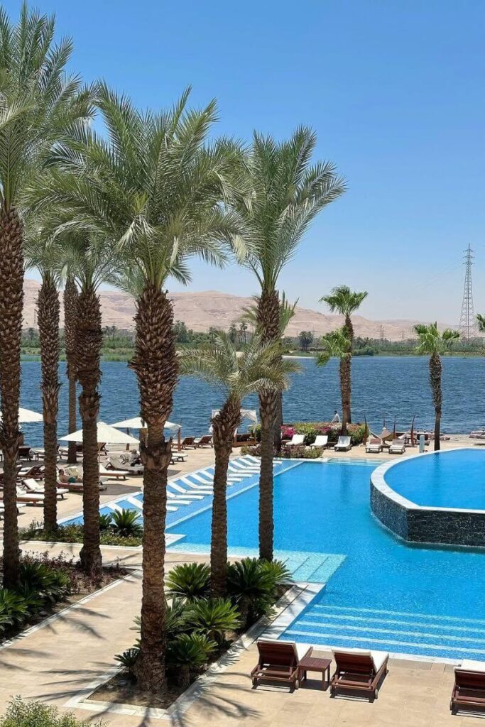 Expansive infinity pool overlooking the Nile River and desert hills in Luxor, framed by palm trees, hammocks, and plush lounge chairs. The resort’s modern design and tranquil riverfront setting position it among the best 5-star hotels in Luxor. Perfect for honeymooners or luxury seekers exploring where to stay in Luxor for the first time.