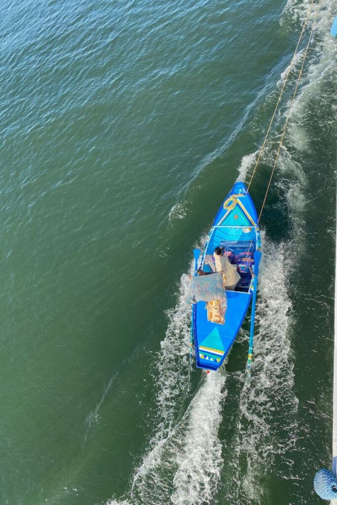 Bright blue local rowboat trailing alongside a Nile cruise ship, with a man selling goods—great for cultural travel stories or Nile cruise from Aswan to Luxor highlights.