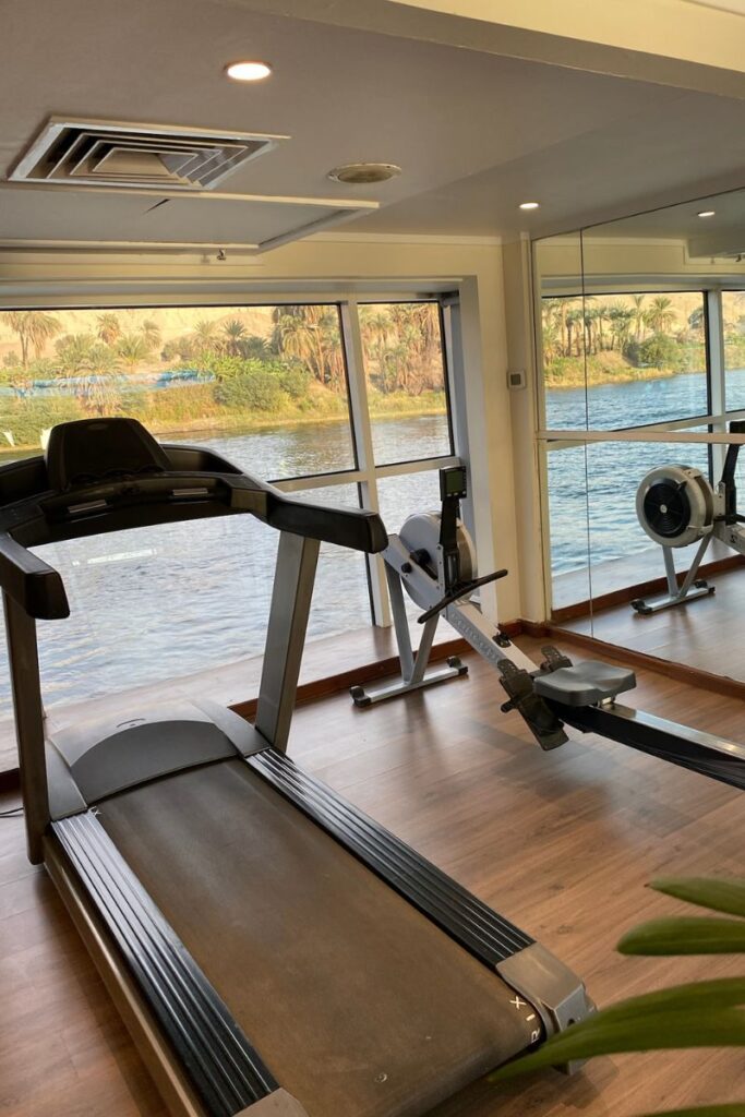 Onboard gym with a treadmill and rowing machine facing large windows with views of the Nile River—perfect for fitness amenities on the best rated river cruises or luxury Nile cruise ships.