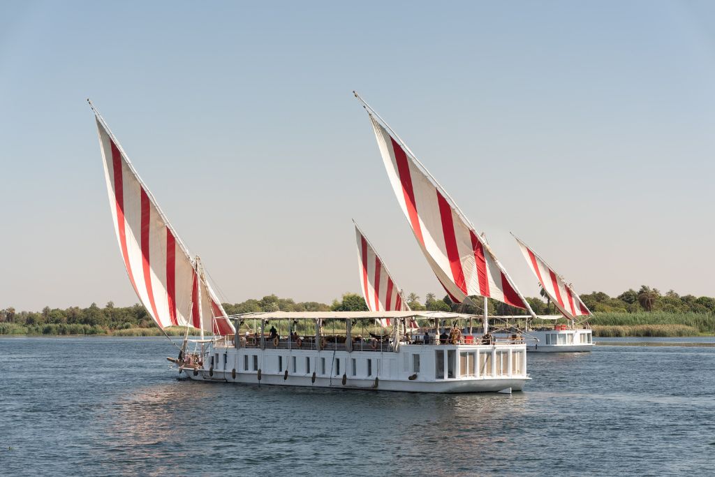 Two traditional dahabiya Nile cruise boats with striking red-and-white striped sails gliding along the Nile—ideal image for posts on dahabiya Nile cruises or Nour El Nil luxury experiences.