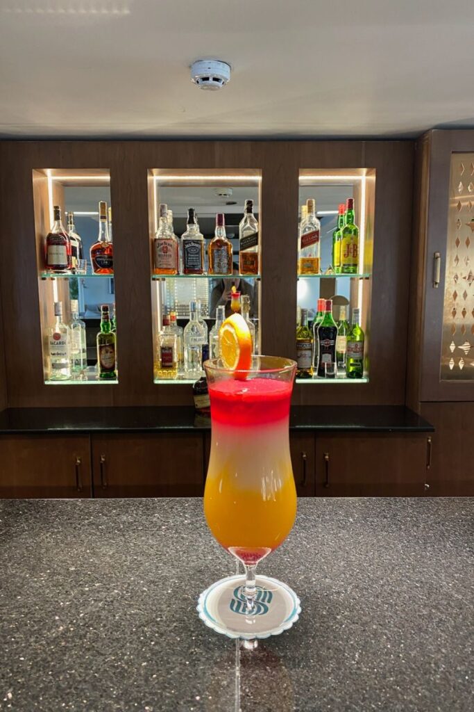 A vibrant layered cocktail with an orange garnish on a bar counter, surrounded by top-shelf liquor on a Nile cruise ship—excellent for river Nile dinner cruise or luxury Nile cruise lounge content.