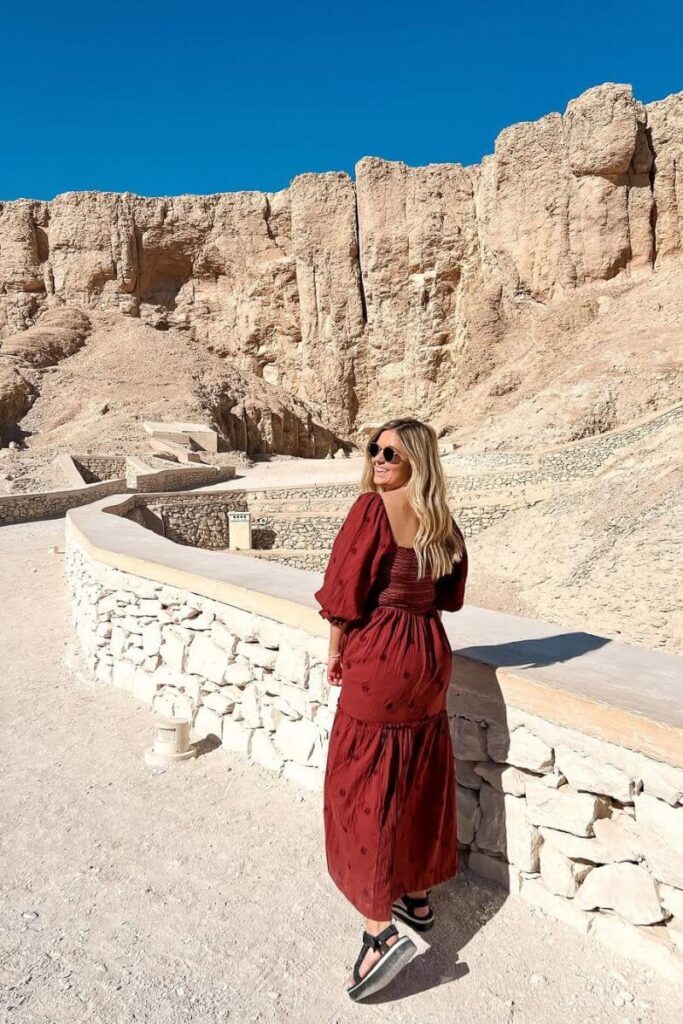 A woman in a red dress explores the sunlit pathways of the Valley of the Kings surrounded by rugged desert cliffs. One of the most iconic Luxor attractions and a key highlight for visitors wondering what to see in Luxor.