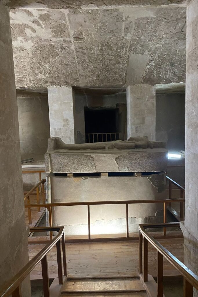 This image of Luxor Valley of the Kings tombs shows a descending staircase bordered by wooden railings, leading into a chamber with walls adorned in hieroglyphs and detailed depictions of Egyptian figures. The warm golden lighting highlights the depth of the carvings, immersing visitors in the grandeur and history of these ancient burial sites.
