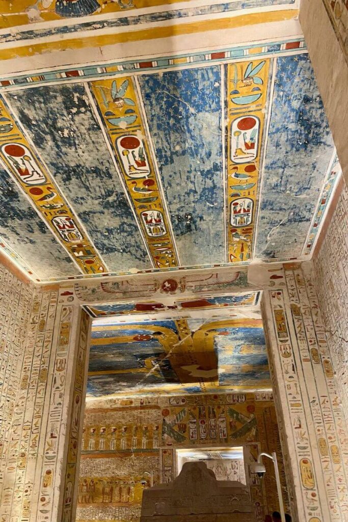 The photo from Luxor Valley of the Kings tombs captures a corner where the vibrant murals and hieroglyphs cover the walls and ceiling. Blue and gold celestial designs adorn the ceiling, while the walls feature rows of figures and symbols. This intricate art showcases the ancient Egyptians' deep spiritual beliefs and their sophisticated tomb decoration techniques.
