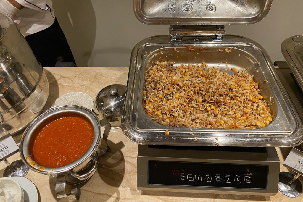 Traditional Egyptian dish koshari served buffet-style with a side of tomato sauce. A delicious highlight for foodies wondering what to eat in Aswan, Egypt during their visit.
