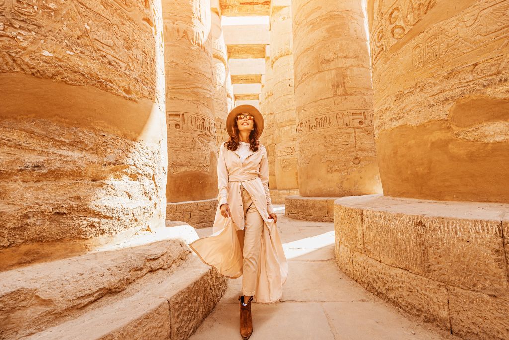 Stylish woman walking through the massive stone columns of Karnak Temple in Luxor, Egypt—ideal for blog posts about what to wear on a Nile cruise or combining Egypt tours with Nile cruises.