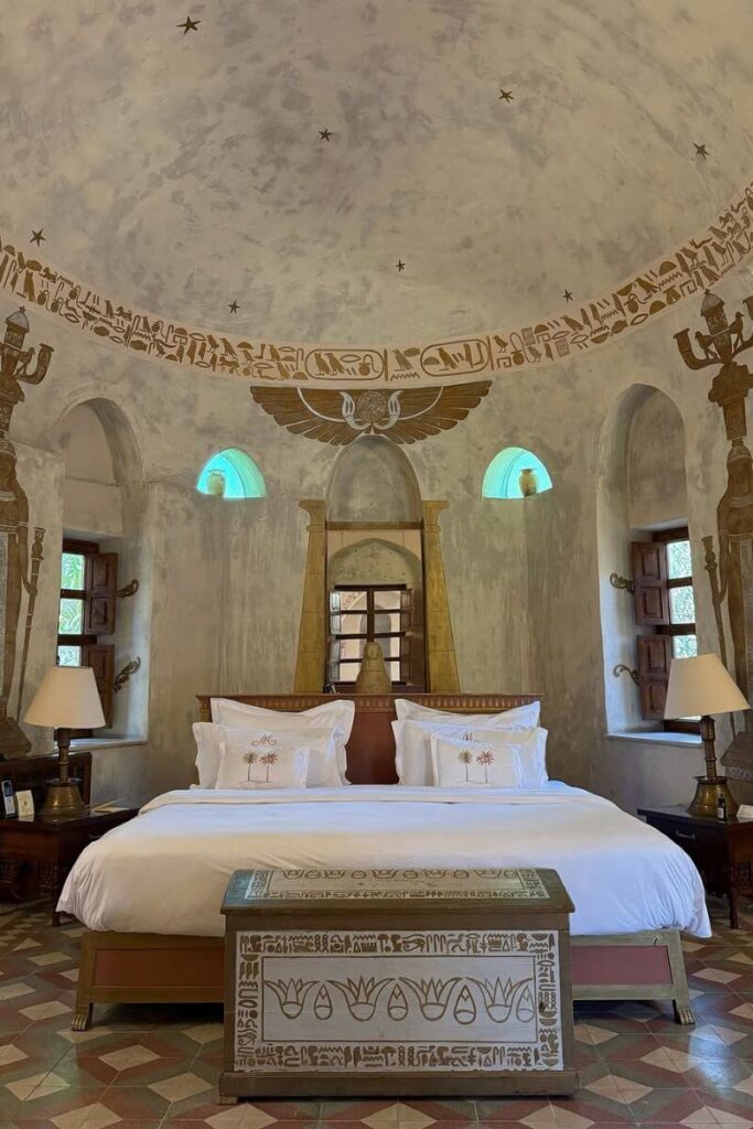 Luxurious hotel room in Luxor decorated with ancient Egyptian motifs, including hieroglyphics and winged sun disk artwork above the bed. This themed stay offers a unique base for exploring the Valley of the Kings tombs.