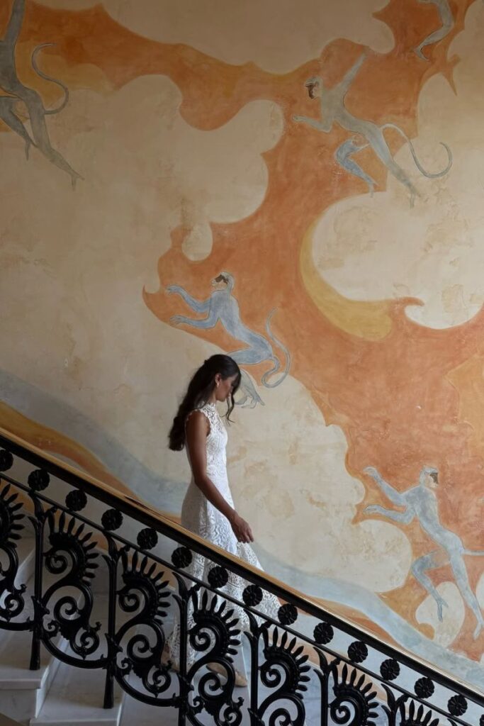 Woman in a white lace dress walking down a staircase in front of a mural with playful monkeys and swirling clouds. Captured in one of the best hotels in Hurghada for couples and an artistic example of boutique hotels in Hurghada Egypt.