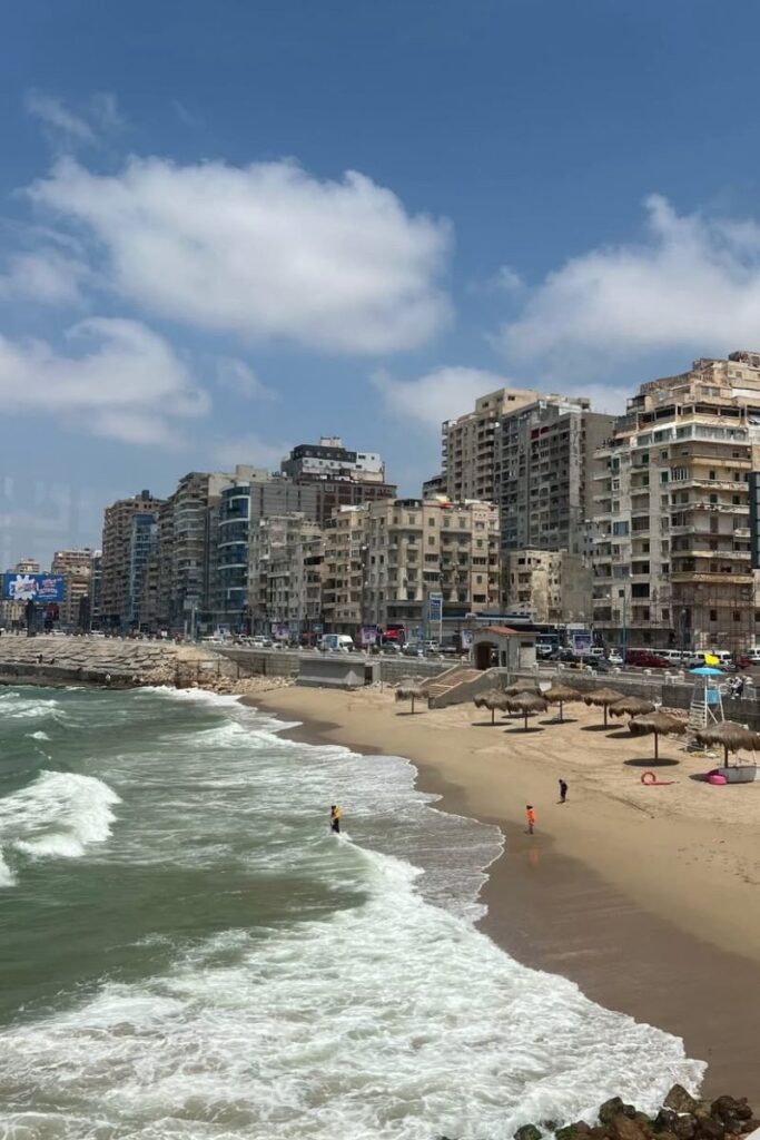 Urban beach in Alexandria, lined with apartment buildings and people enjoying the surf, showcasing one of the best cities to visit in Egypt. This blend of coast and city makes it one of the most accessible Egyptian beaches near Cairo.