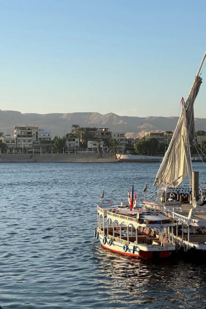 Colorful boats docked along the Nile River at sunset, backed by palm trees and desert hills. A tranquil experience in Egypt and one of the most scenic places to visit in Egypt for river cruises.