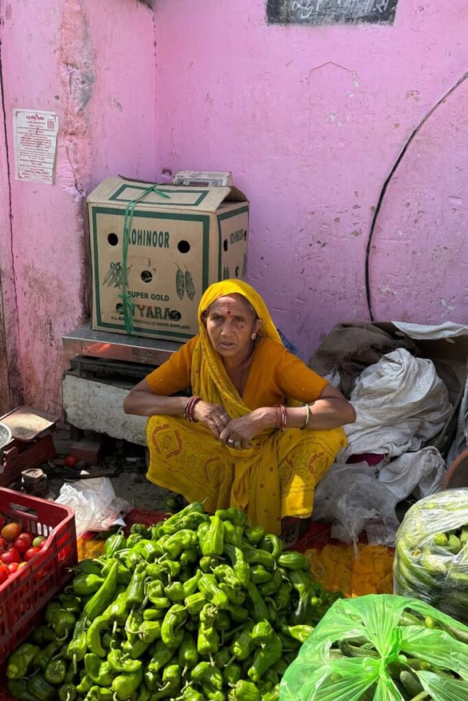 woman in a bright yellow sari sitting beside a display of green bell peppers at a market in India. Excellent for discussing best solo travel destinations India, or best destinations for solo female travelers seeking cultural experiences.