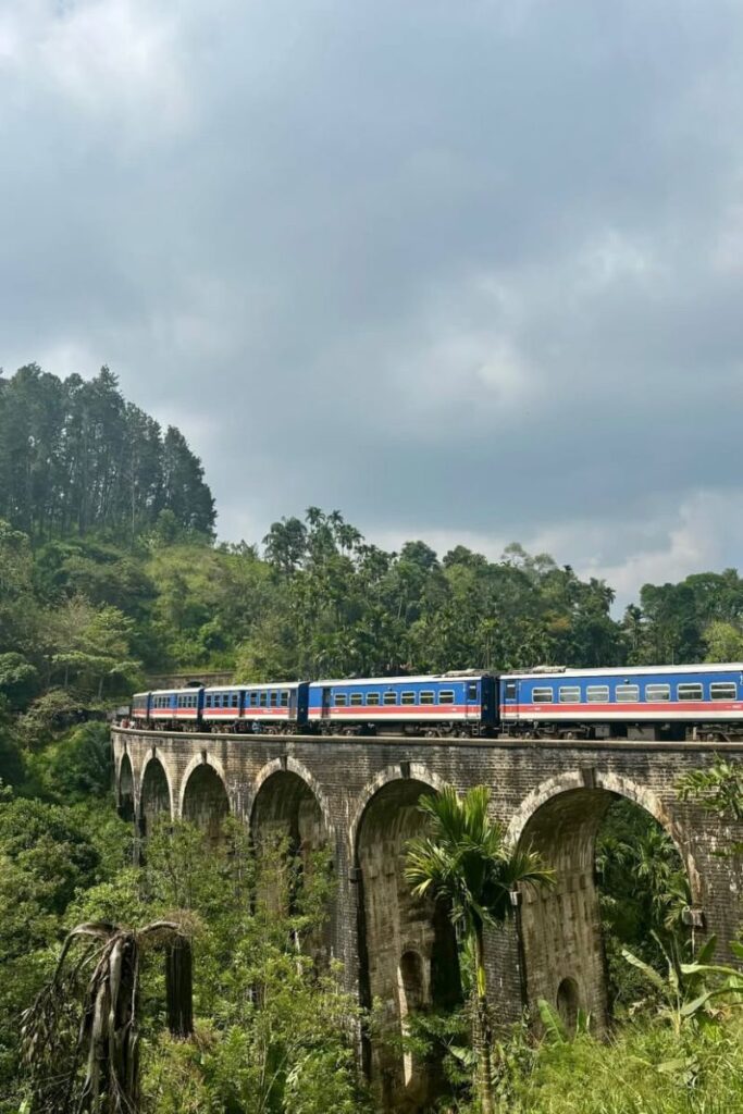 A colorful train crossing the Nine Arches Bridge in Sri Lanka, surrounded by lush green forest and cloudy skies. Ideal for posts about solo female travel Sri Lanka or best place for solo travel in Europe-style scenic escapes.
