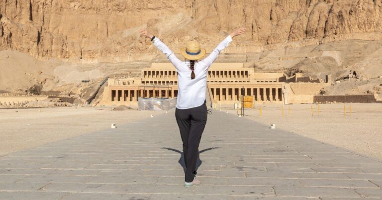 A traveler standing with arms outstretched in front of Hatshepsut Temple carved into cliffs in Luxor. One of the top 10 places to visit in Egypt and a striking example of ancient Egypt landmarks.