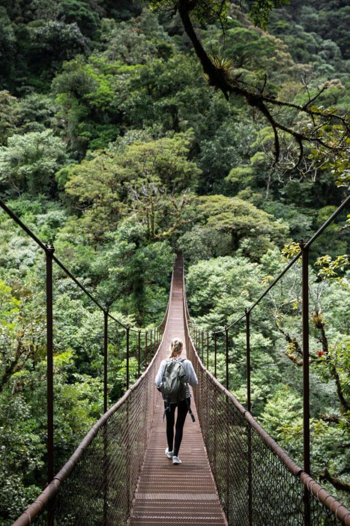 A woman walks alone across a suspension bridge in a lush Costa Rican cloud forest, showcasing why Costa Rica is one of the best places for solo women travelers seeking adventure, especially for first time solo female travel.