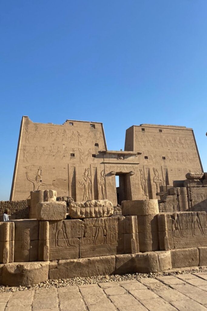 Temple of Edfu with high walls covered in ancient carvings of gods and pharaohs, set against a blue sky. This is one of the best preserved landmarks of ancient Egypt and a top experience in Egypt for history lovers.
