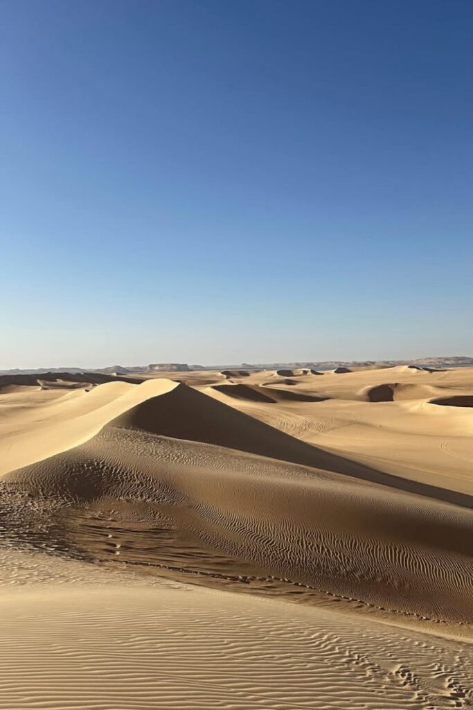Golden dunes of the Egyptian desert stretching across the horizon, offering a peaceful and vast view. A beautiful place to visit in Egypt for adventurous experiences in Egypt.