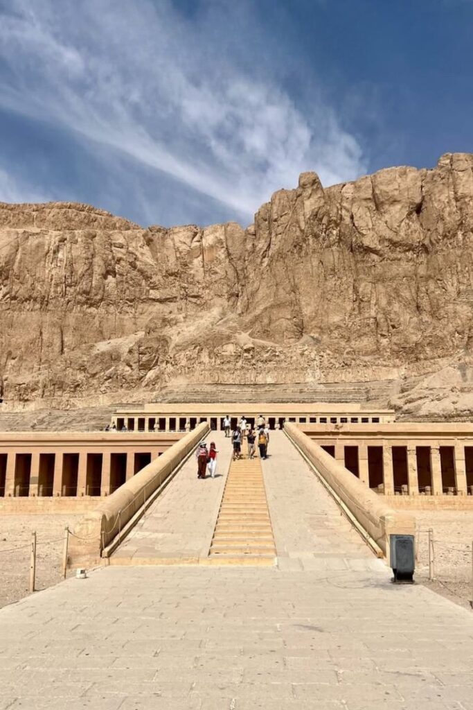 Wide stone walkway leading to the Temple of Hatshepsut, nestled against a dramatic cliff backdrop, one of the most famous temples in Egypt and a key stop on the list of ancient Egyptian temples.