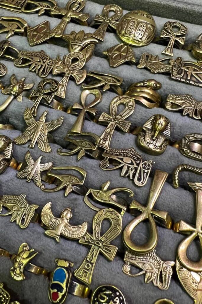 A close-up of gold rings and symbols including ankhs, eyes of Horus, pharaoh heads, and scarabs, beautifully laid out in a velvet display case. These pieces exemplify the fine detail and cultural significance of Egypt gold jewelry and are top picks for anyone shopping for Egyptian gold chains or considering buying gold in Egypt. Perfect for those interested in gold shops in Egypt and authentic historical souvenirs.