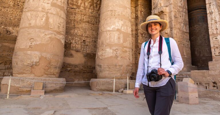 A female tourist stands with a camera around her neck at an ancient Egyptian temple, surrounded by massive sandstone columns covered in hieroglyphs. A reassuring image for women travelers in Egypt and those questioning is Egypt safe for women?